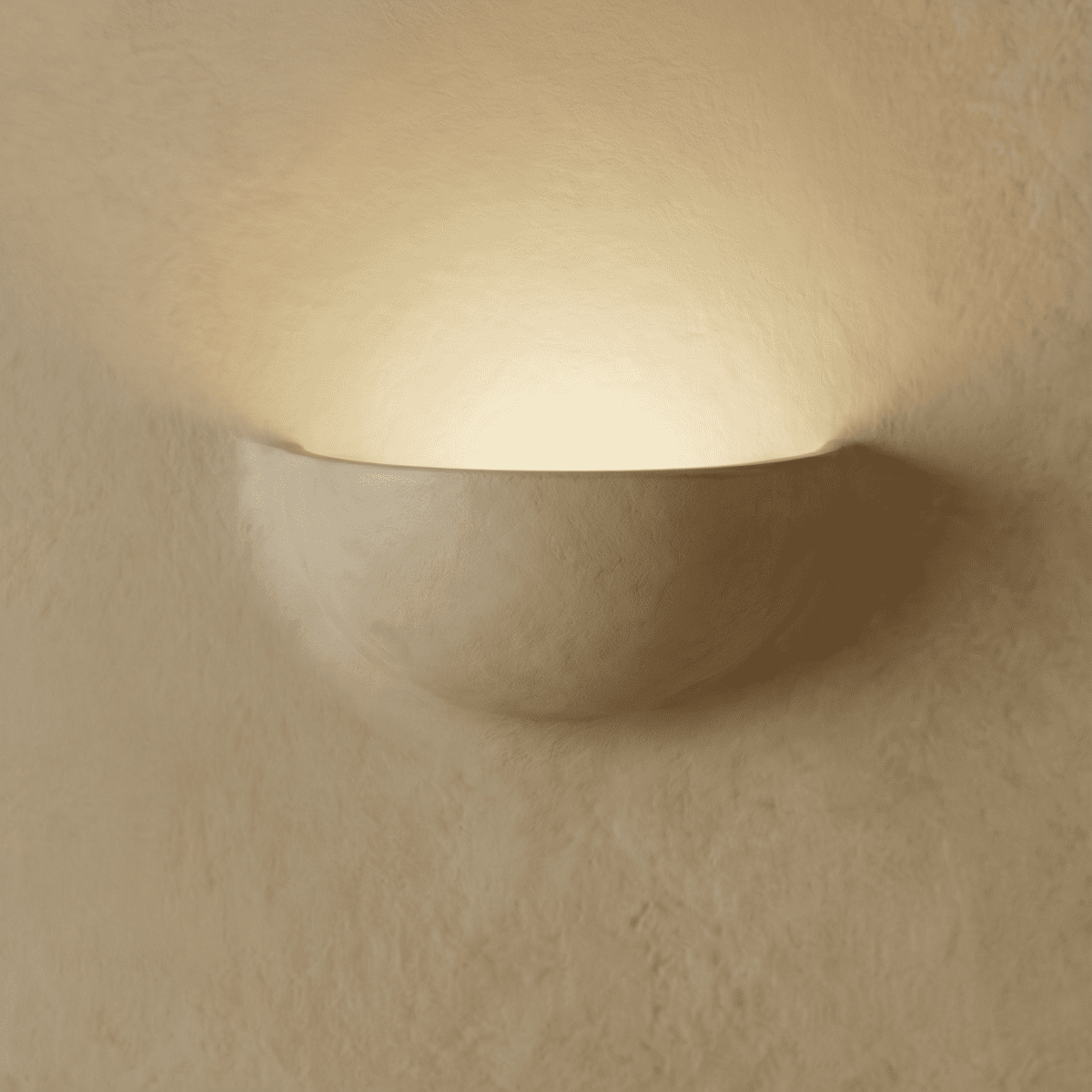 Clérachic half-moon plaster wall light glowing upward on a limewashed wall, its matte white shell casting a warm halo.