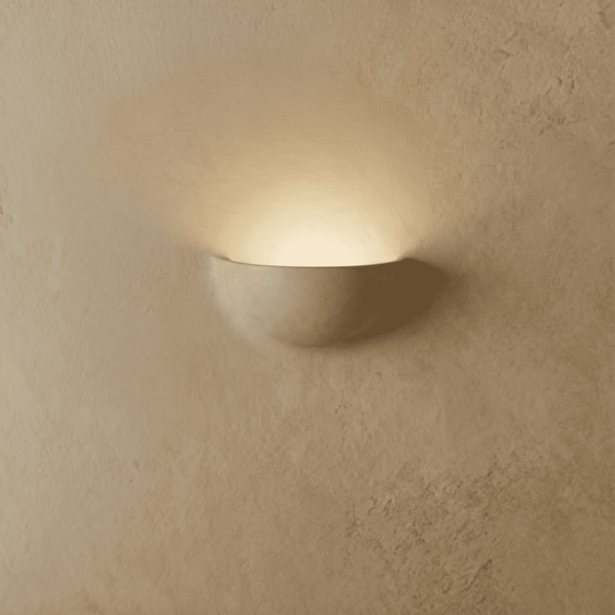 Clérachic half-moon plaster wall light in matte white lit from within, throwing a soft arc of light up a textured wall.