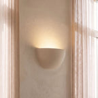 Clérachic half-moon plaster wall light lit on a plastered wall between sheer curtains and a tall window.