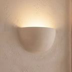 Close view of the Clérachic half-moon plaster wall light, a smooth matte white shell with light washing up the wall.