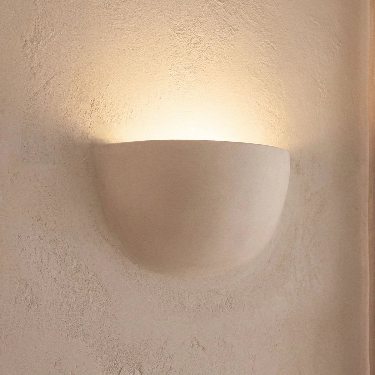 Close view of the Clérachic half-moon plaster wall light, a smooth matte white shell with light washing up the wall.