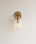 Clérachic brushed gold wall sconce with a knurled bracket and clear glass cylinder shade around a filament bulb.