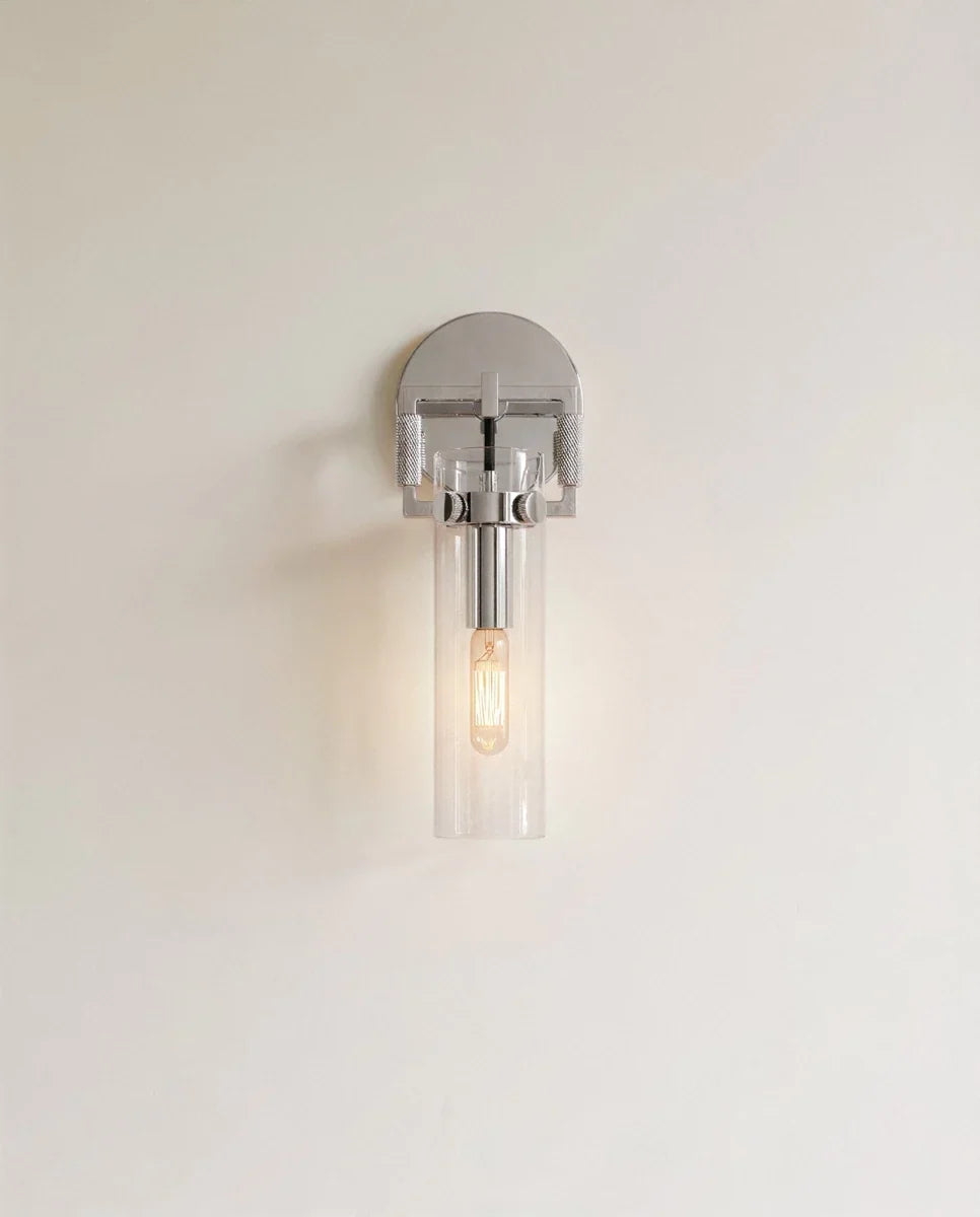 Clérachic polished chrome wall sconce with a clear glass cylinder shade and a warm filament bulb on a pale wall.