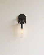 Clérachic black wall sconce with a half-round backplate, clear glass cylinder shade and a lit filament bulb.