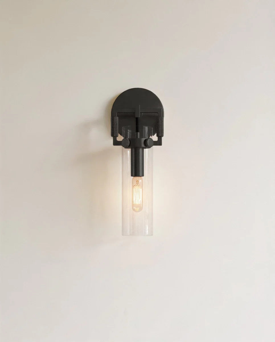 Clérachic black wall sconce with a half-round backplate, clear glass cylinder shade and a lit filament bulb.