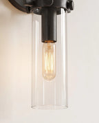 Clérachic close view of the black sconce, a clear glass cylinder shade around a glowing tube filament bulb.