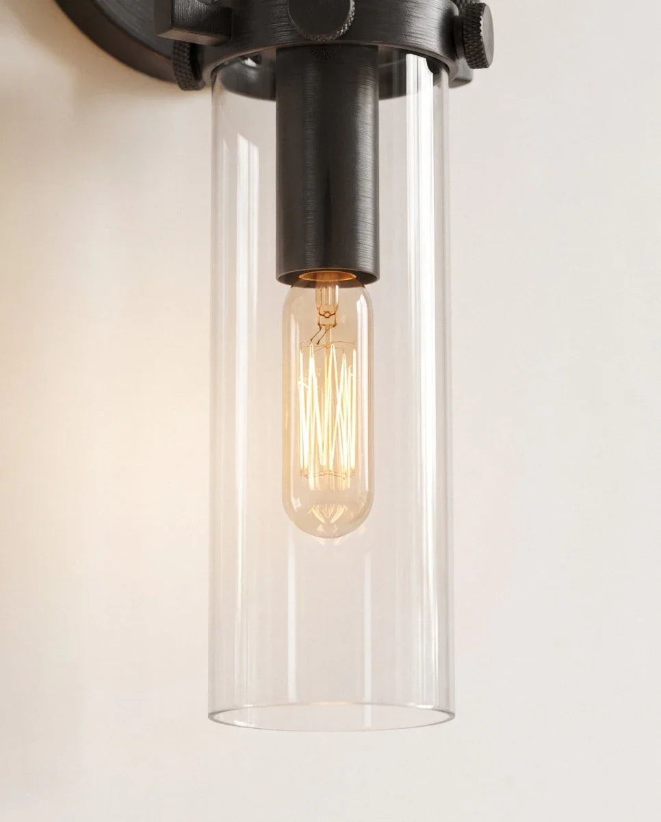 Clérachic close view of the black sconce, a clear glass cylinder shade around a glowing tube filament bulb.