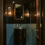 Clérachic pair of chrome glass-cylinder sconces flanking a beaded wooden mirror in a dark tiled room.