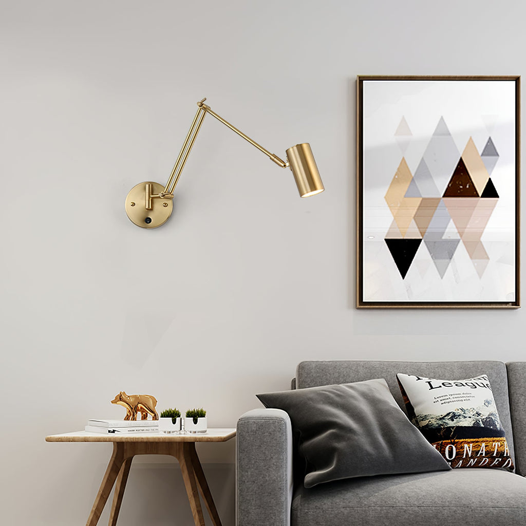 A gold Clérachic wall light with a slim cylinder head and a long swing arm above a side table, beside a framed geometric print and a grey sofa.