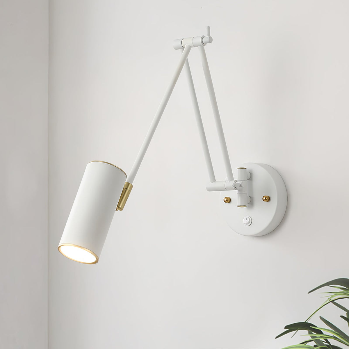 Close view of a white version of the Clérachic wall light, with a cylinder head, gold joints and a round backplate on a white wall.