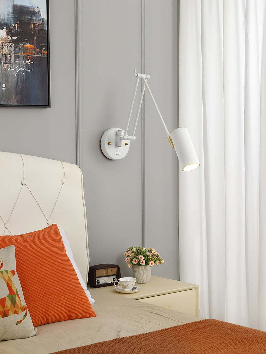 A white version of the Clérachic wall light with a cylinder head above a cream tufted headboard, an orange cushion and a small bedside table.