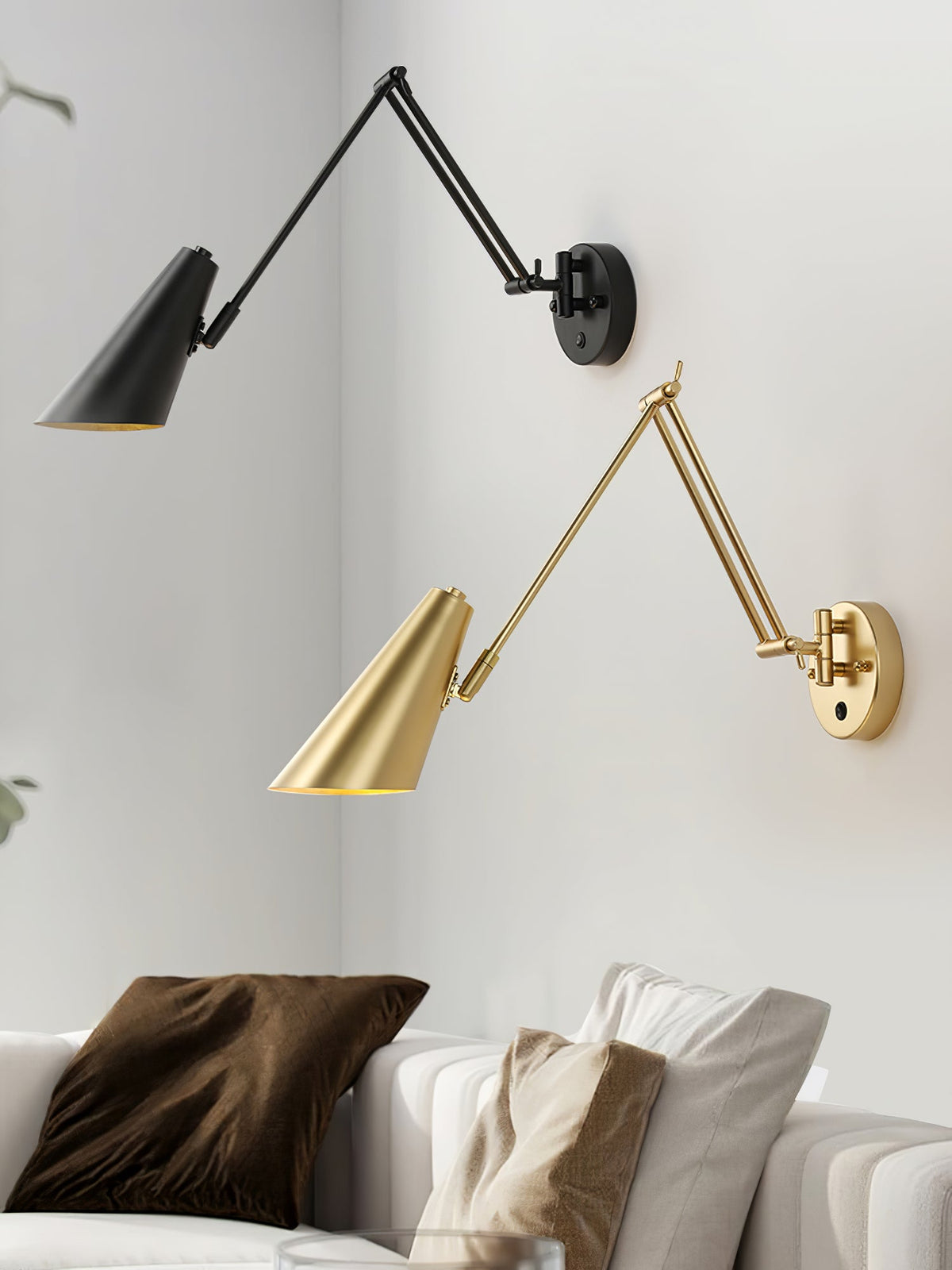 One black and one gold Clérachic swing-arm wall light with conical shades on a white wall above a sofa with brown cushions.