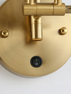 Close view of the round gold backplate on this Clérachic wall light, showing the rocker switch, two screw caps and the arm joint.