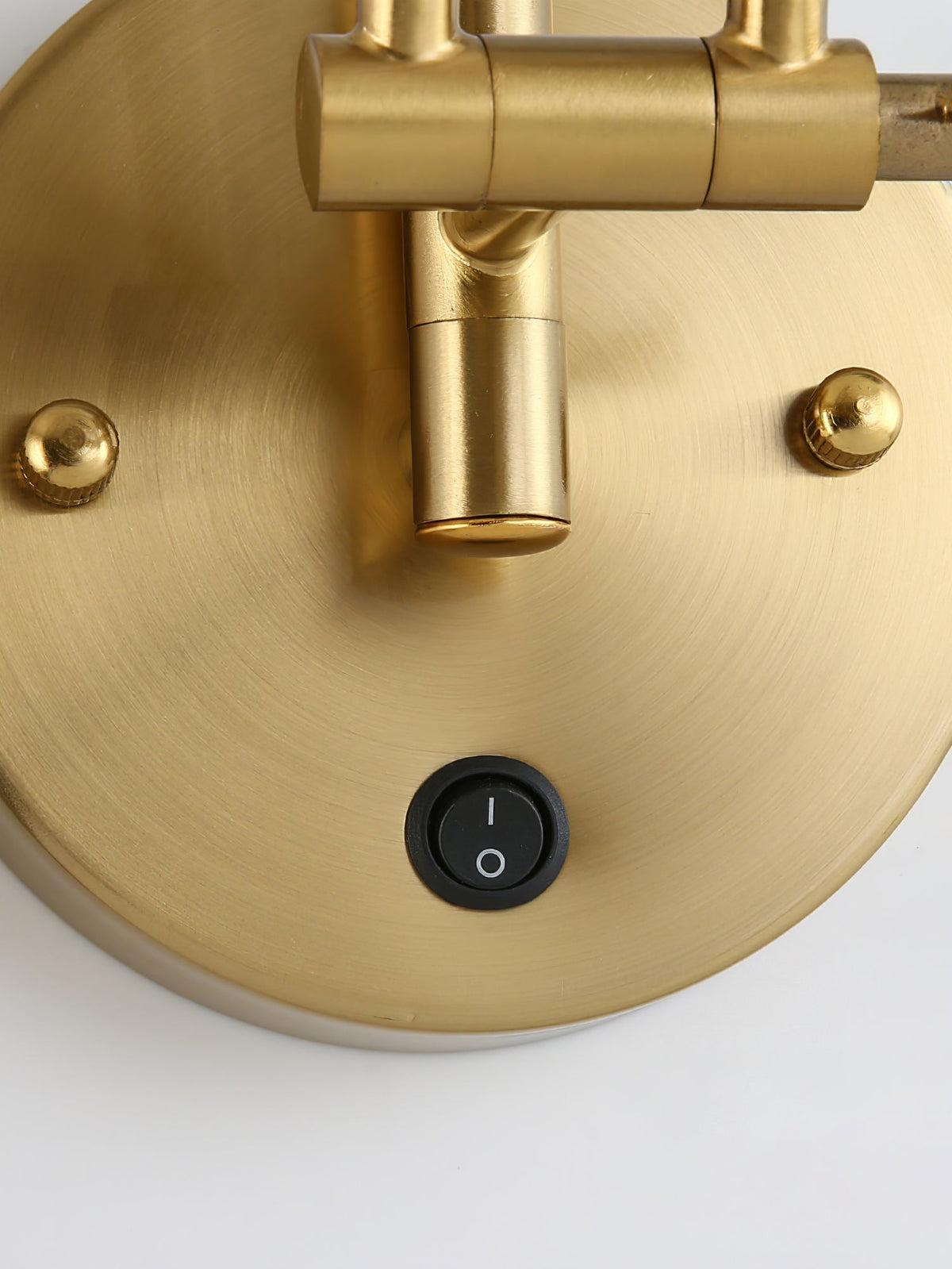 Close view of the round gold backplate on this Clérachic wall light, showing the rocker switch, two screw caps and the arm joint.