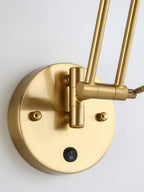 Close view of the round gold backplate, the rocker switch and the swivel base of the double arm on this Clérachic wall light.