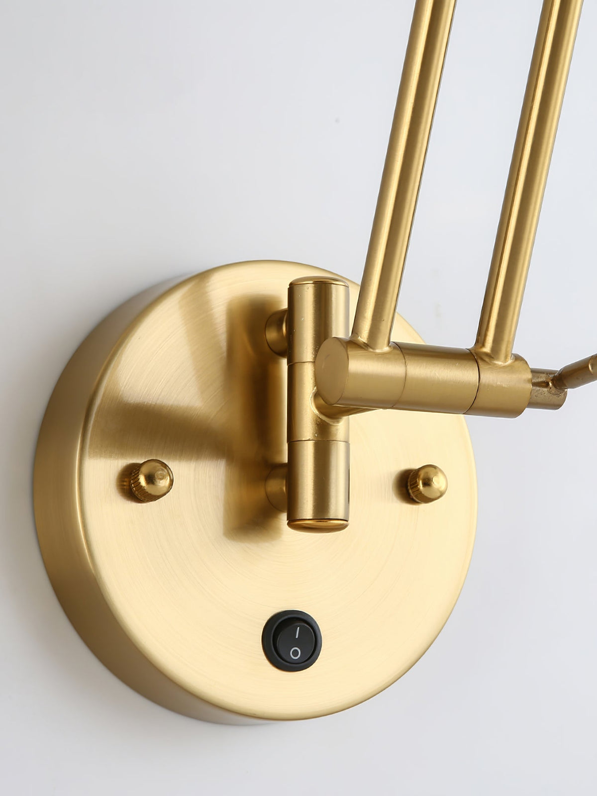 Close view of the round gold backplate, the rocker switch and the swivel base of the double arm on this Clérachic wall light.