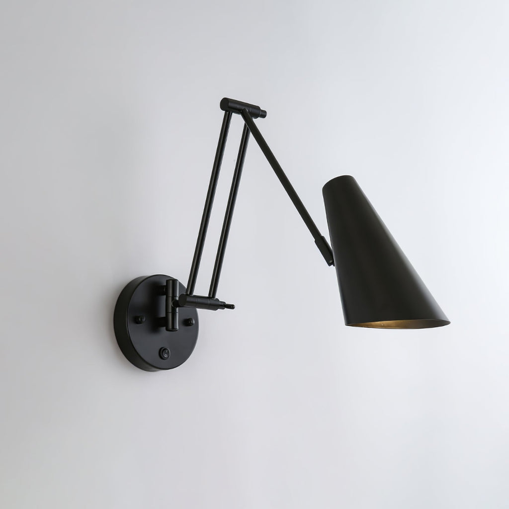 A Clérachic wall light in black, with a conical shade on a folded arm reaching to the right of its round backplate.