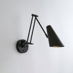 A Clérachic wall light in black, with a conical shade on a folded arm reaching to the right of its round backplate.