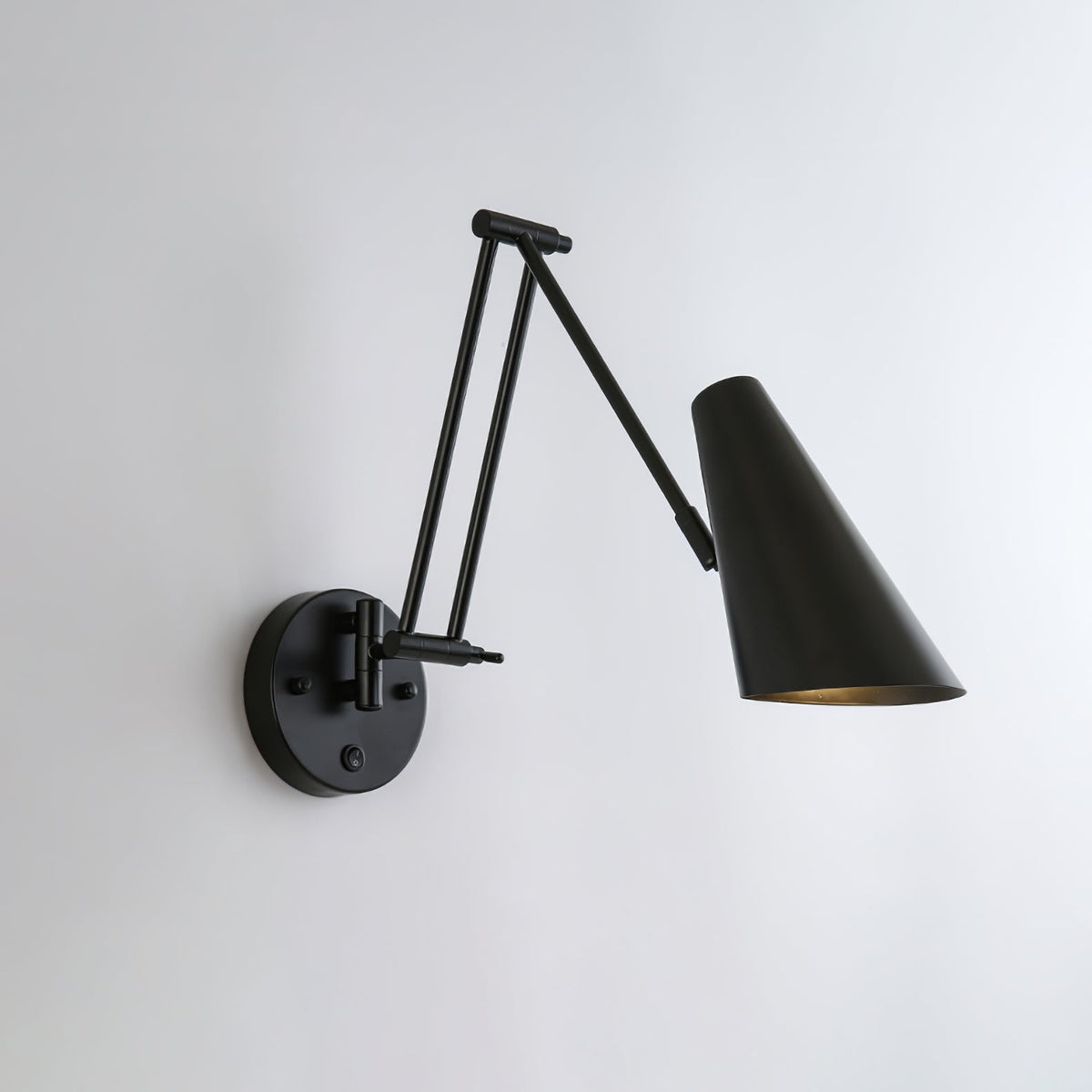 A Clérachic wall light in black, with a conical shade on a folded arm reaching to the right of its round backplate.