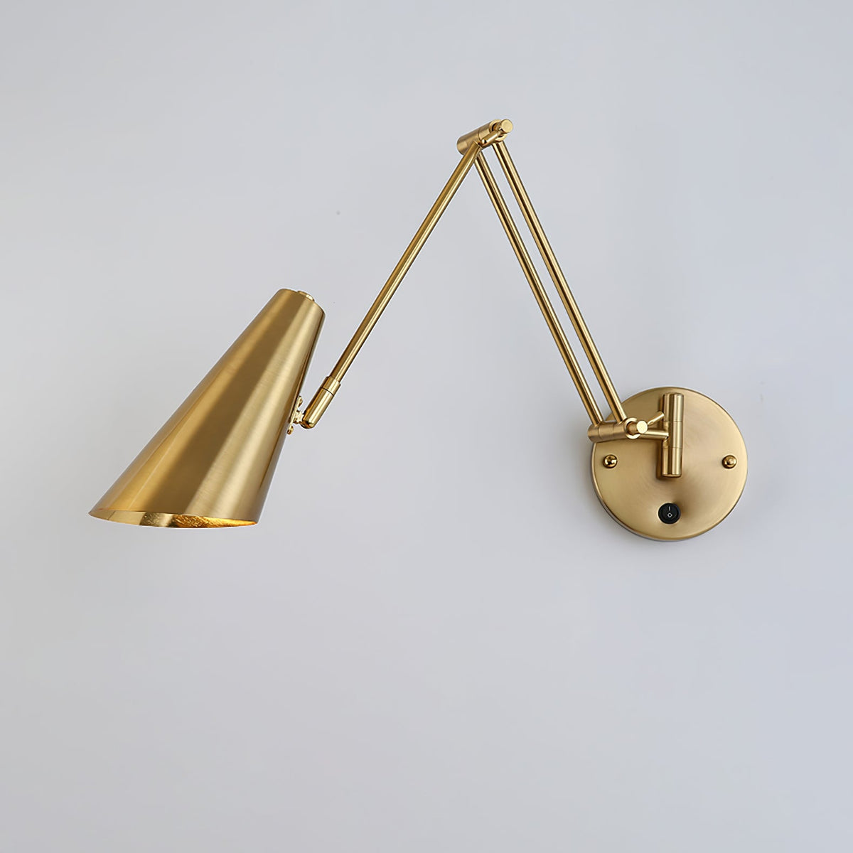 Gold Clérachic wall light with a conical shade reaching to the left, the arm folded back to a round backplate with a switch.