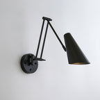 Clérachic black wall light with a large conical shade held out on a folded arm, on a pale grey wall.