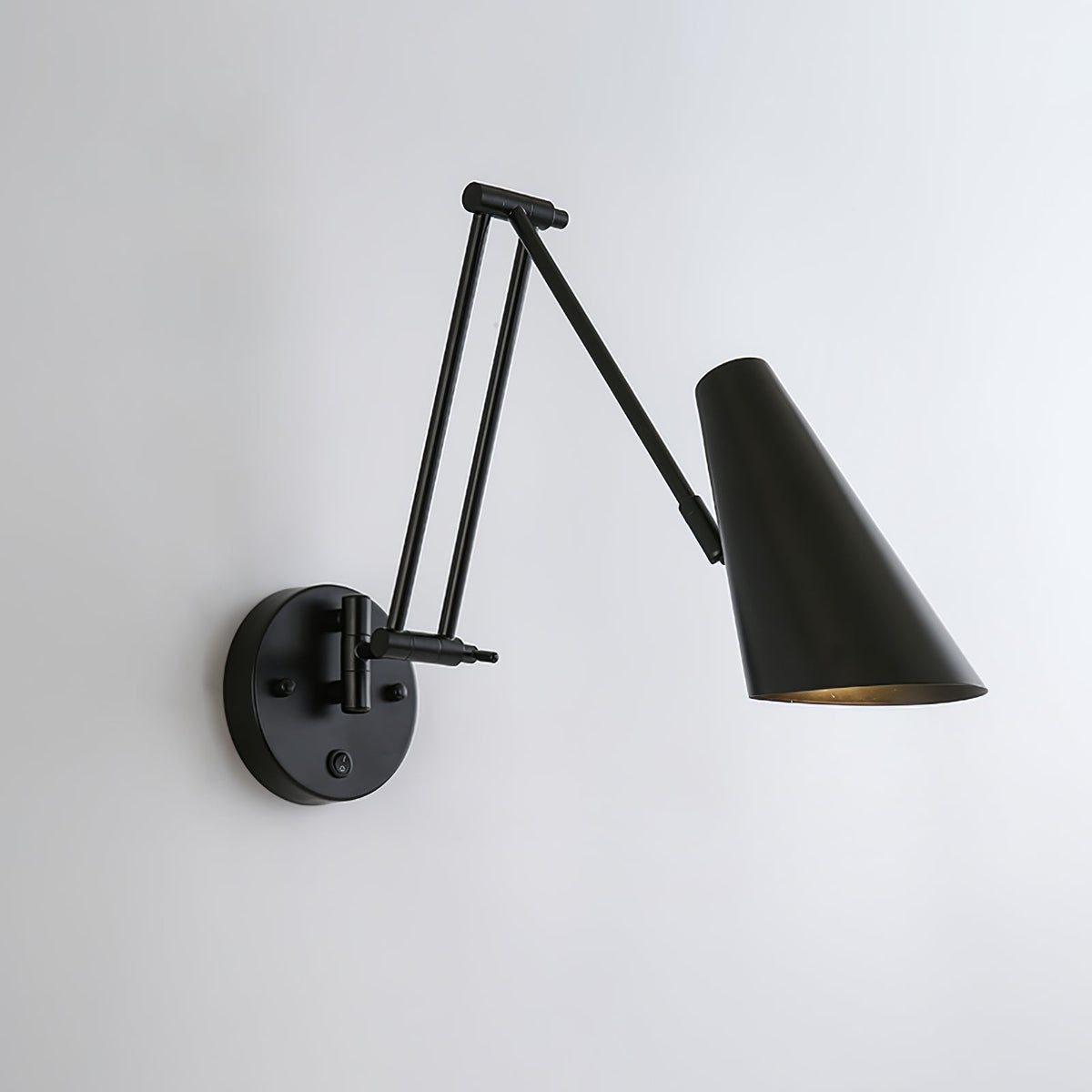 Clérachic black wall light with a large conical shade held out on a folded arm, on a pale grey wall.