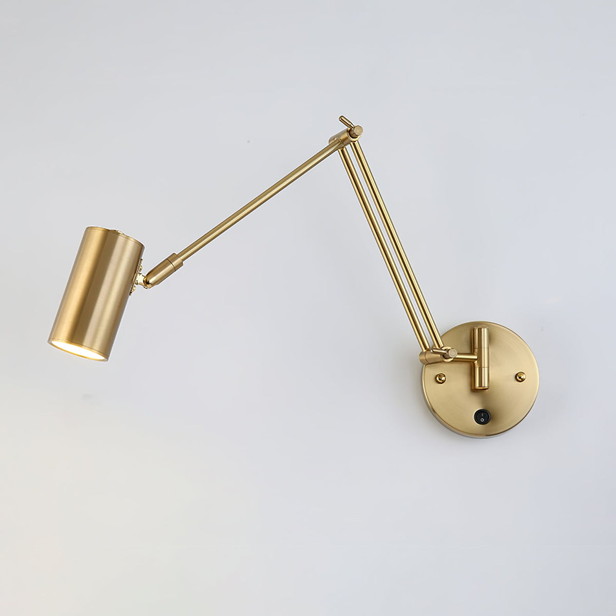 Gold Clérachic swing-arm wall light with a small cylinder head extended to the left on a long arm, against a light wall.