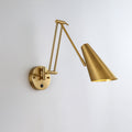 A gold Clérachic swing-arm wall light with a conical shade held out to the right of its round backplate, on a pale wall.