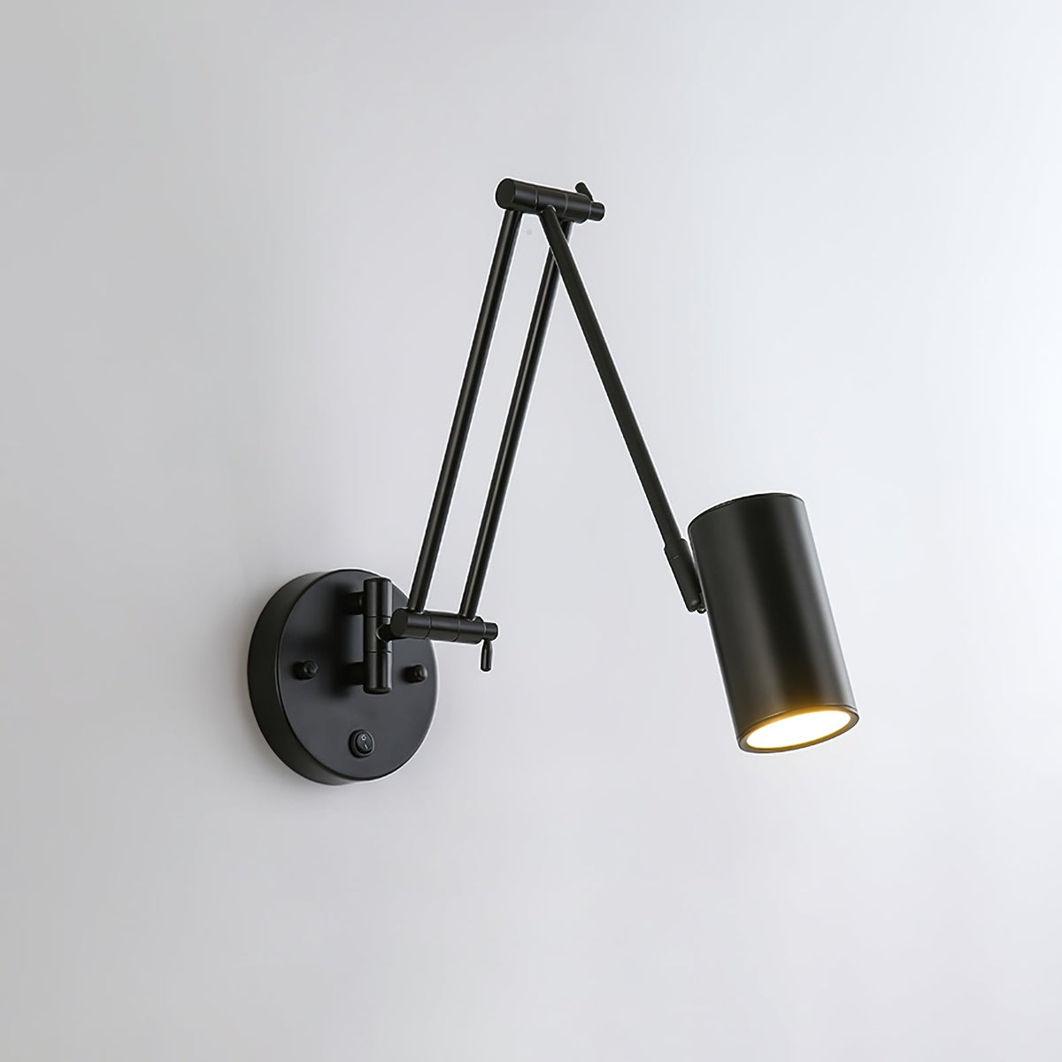 Black Clérachic wall light with a cylinder head on a folded double arm and a round backplate, on a pale grey wall.