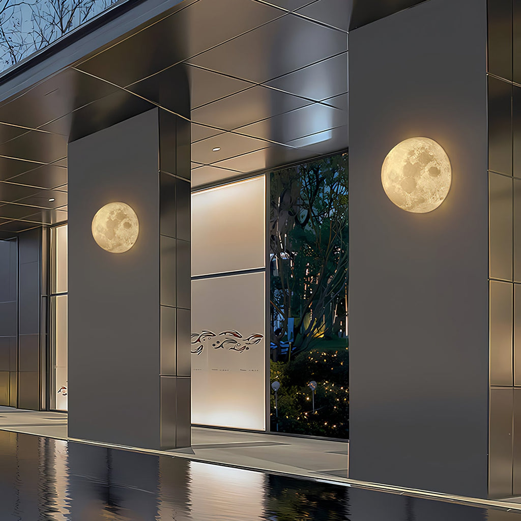 Two round Clérachic moon wall lights on dark cladding columns beside a still pool and a glass entrance.