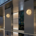 Two round Clérachic moon wall lights on dark cladding columns beside a still pool and a glass entrance.