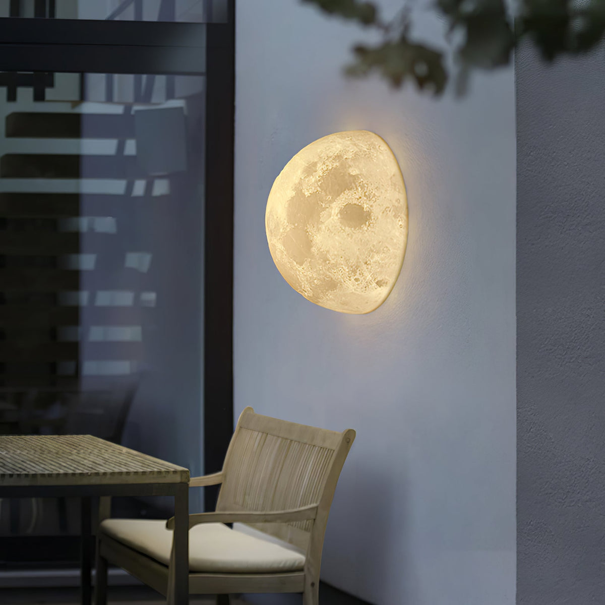 Clérachic half-moon wall light on a grey terrace wall, with a wooden chair and table in front of a dark window.
