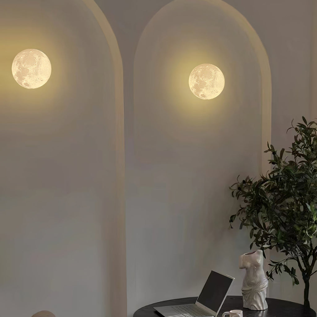 Two round Clérachic moon wall lights set in arched plaster recesses, with a plant and a laptop on a table below.