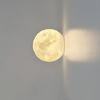 Round Clérachic moon wall light with the cratered surface visible, shown side-on with light cast along the grey wall.