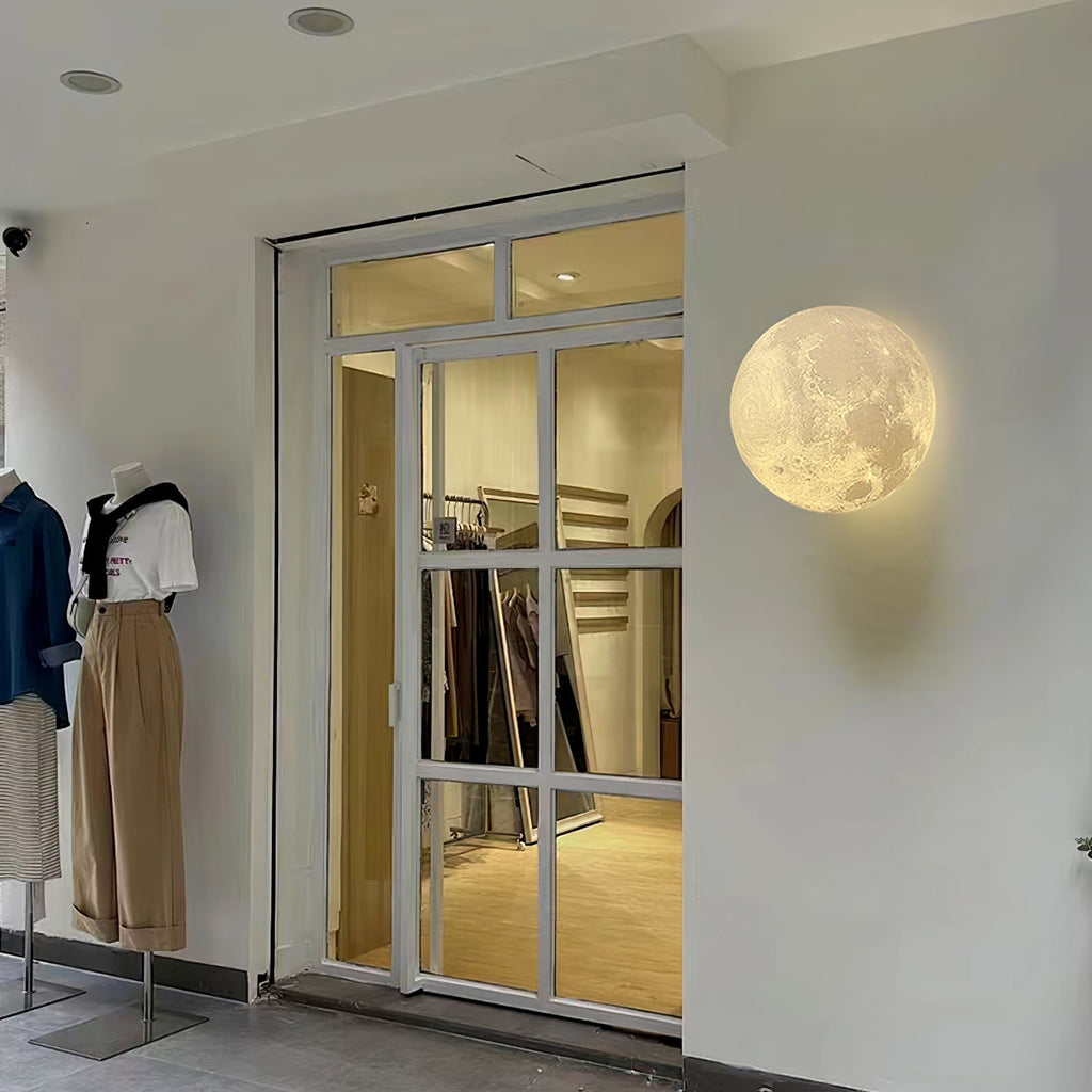 Round Clérachic moon wall light on a white shopfront wall beside a glass door and clothing mannequins.