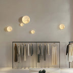 Five small round Clérachic moon lights scattered across a high wall above a clothes rail in a pale boutique.