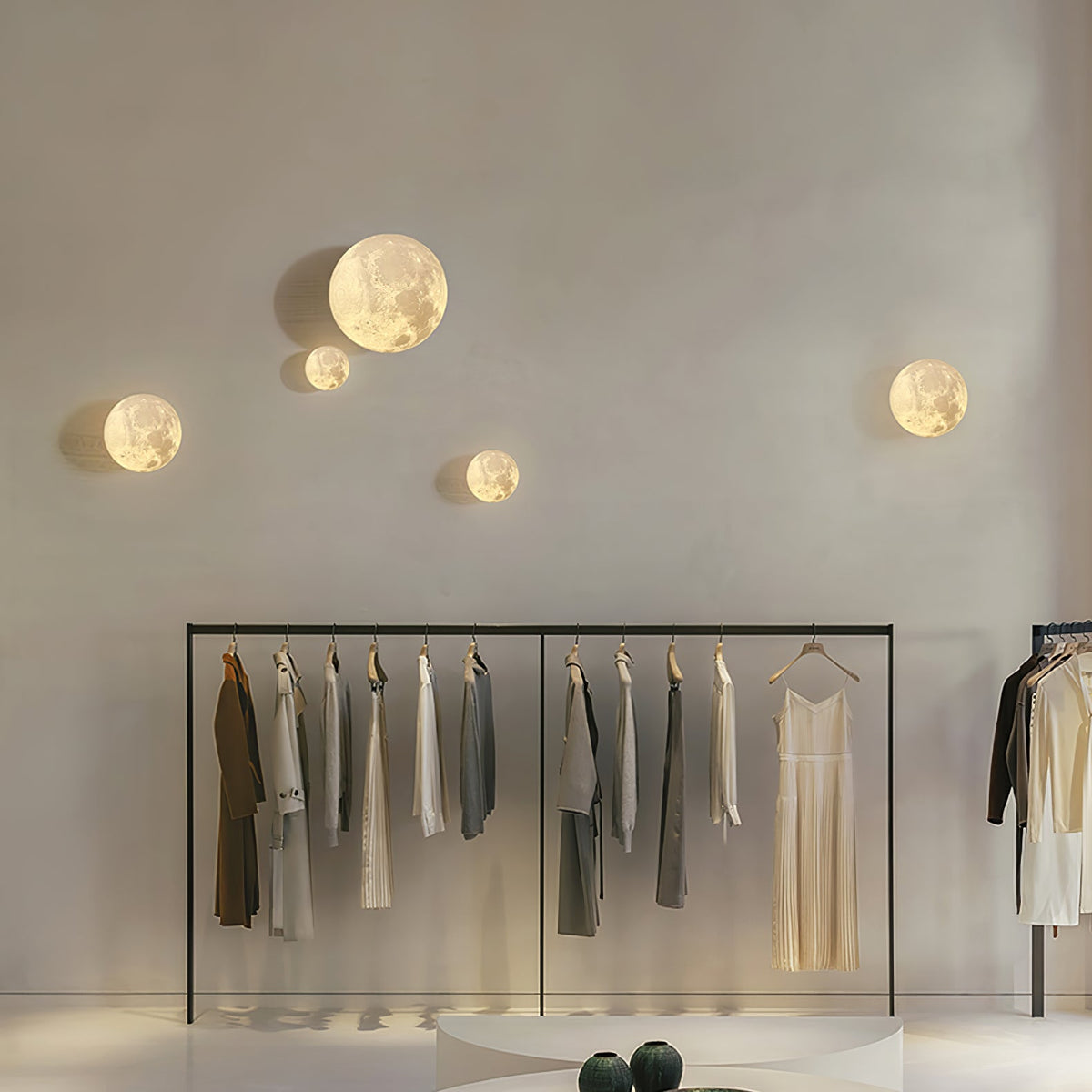 Five small round Clérachic moon lights scattered across a high wall above a clothes rail in a pale boutique.