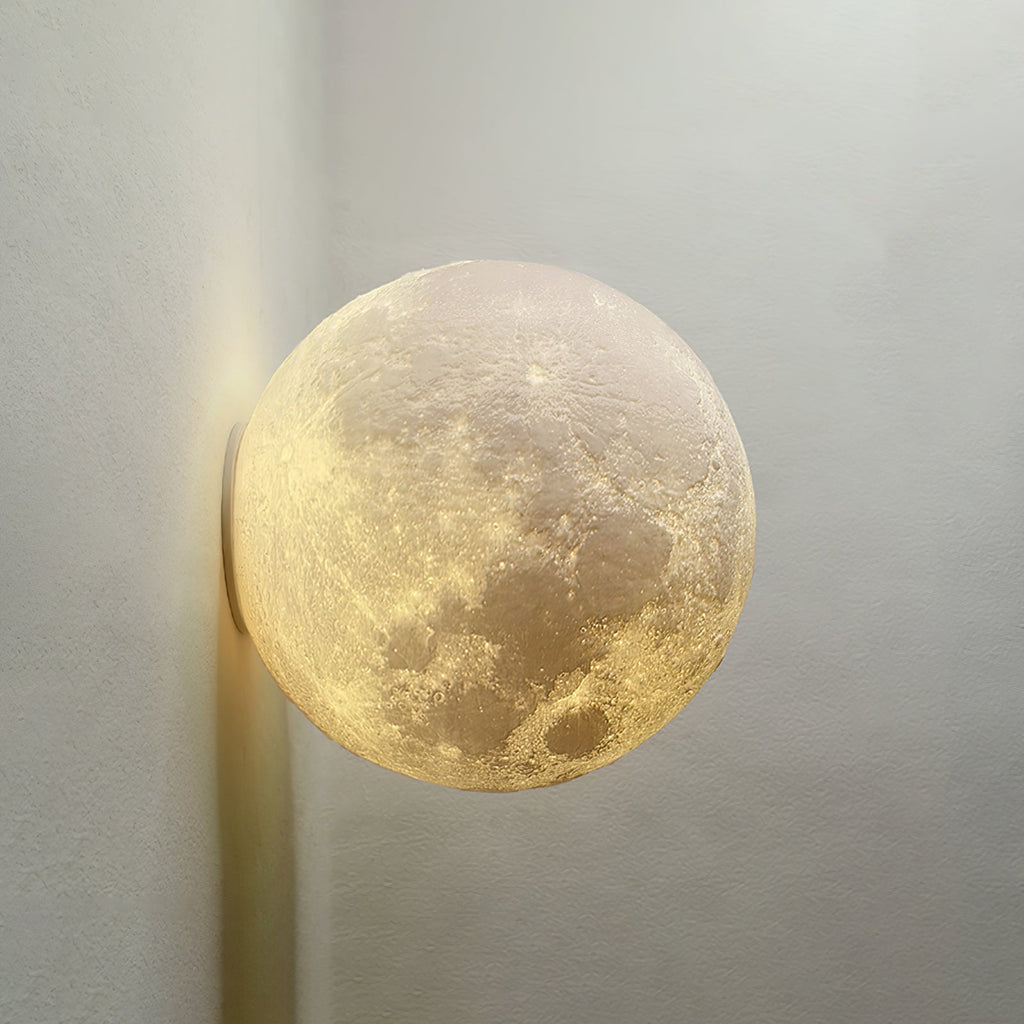 Large round Clérachic moon wall light shown close, its cratered surface lit warmly against a pale grey wall.