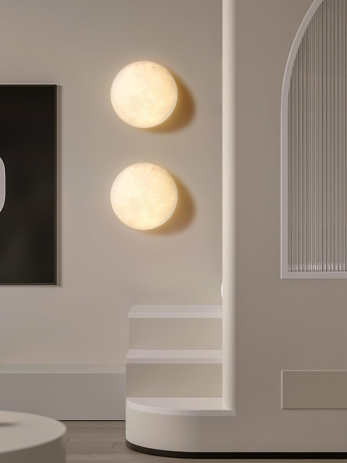 Two round Clérachic moon wall lights, one above the other, on a cream wall beside a curved step and a dark artwork.