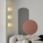 Three small round Clérachic moon wall lights in a column beside a grey and terracotta wall panel, above a white sofa.
