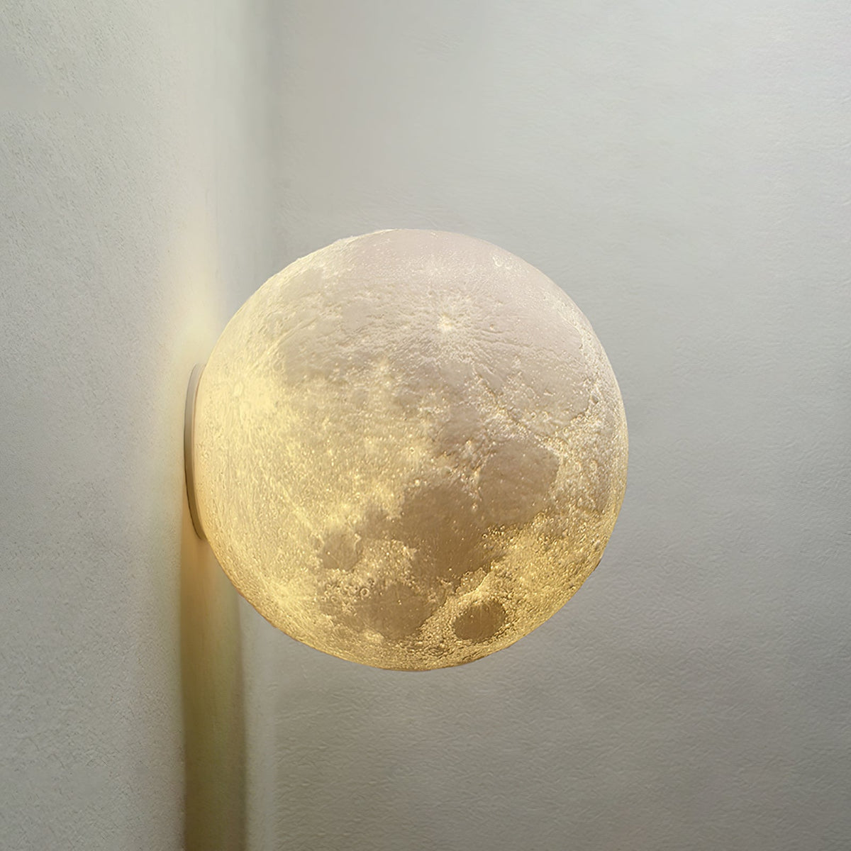 Close view of the cratered surface of a round Clérachic moon wall light, lit warmly against a grey wall.