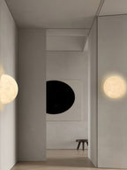 Round Clérachic moon wall light in a plain hallway, with a half-moon on the opposite wall and a dark oval artwork.