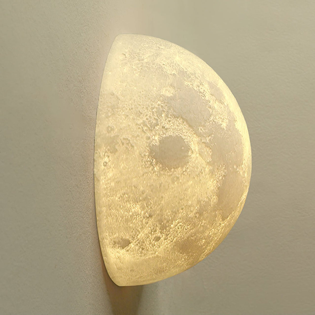 Angled view of a Clérachic half-moon wall light with a warm glow, showing the craters and ridges of its surface.