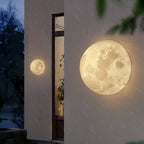 Two round Clérachic moon wall lights on a rendered exterior wall by a tall window, with rain streaks in the dark.
