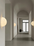 Clérachic half-moon and round moon wall lights along a long, arched white corridor with a glass door at the end.