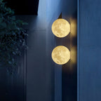 Two round Clérachic moon wall lights, one above the other, glowing on a dark blue concrete wall at night.