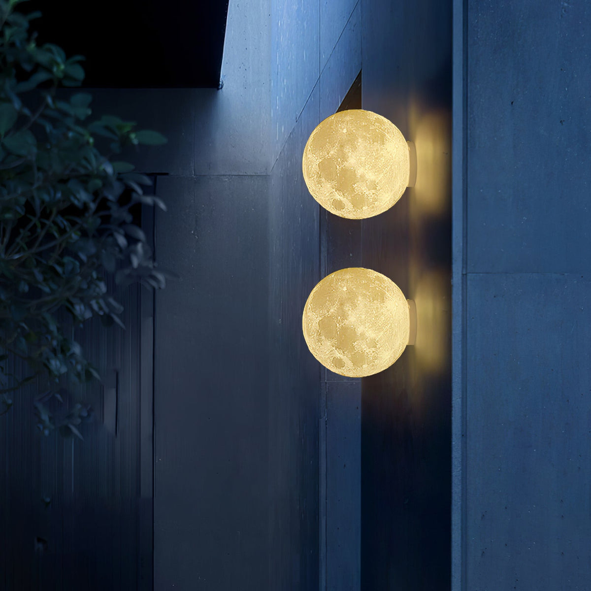 Two round Clérachic moon wall lights, one above the other, glowing on a dark blue concrete wall at night.