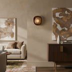 This Clérachic wall light glows softly on a beige wall between two abstract paintings, above a sofa and a dark wood sideboard.