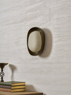 A Clérachic wall light switched off, turned slightly to the side, with a frosted shade, on a pale wall above a stack of books.