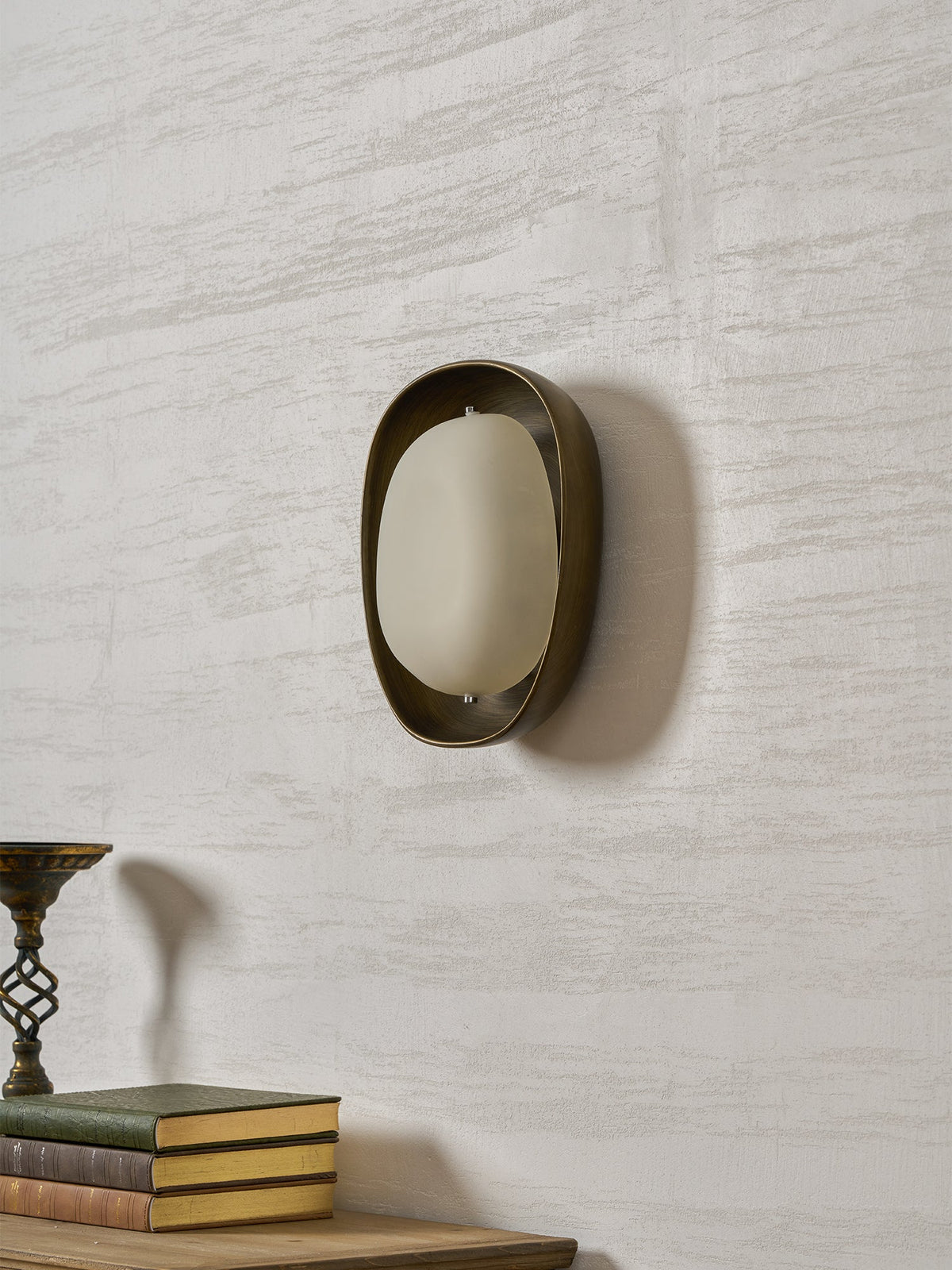 A Clérachic wall light switched off, turned slightly to the side, with a frosted shade, on a pale wall above a stack of books.